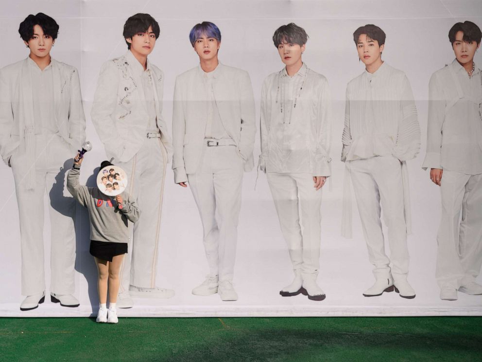 PHOTO: In a photo taken on October 29, 2019, a fan of BTS poses against a backdrop featuring an image of the band members, as they arrive for the final concert of their world tour at the Olympic stadium in Seoul. (Photo by ED JONES/AFP via Getty Images)