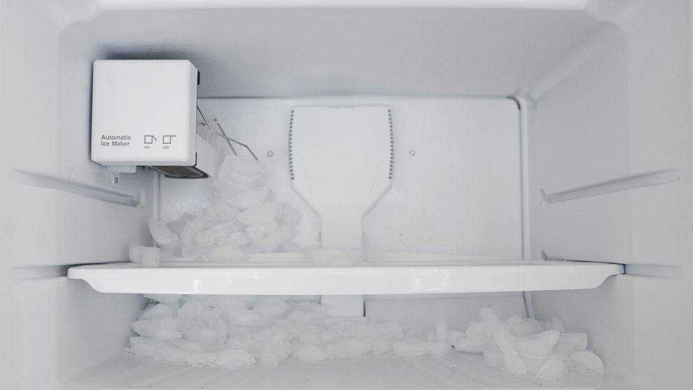 Ice spills out in a fridge as the automatic ice maker malfunctions. 