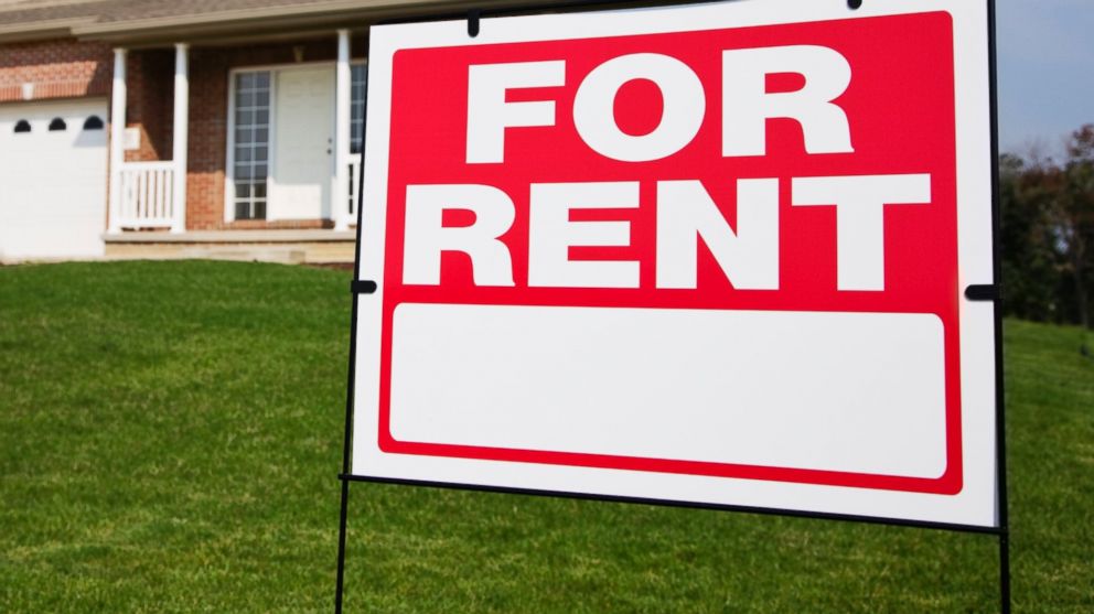 A "For Rent" sign is pictured in front of a home in this stock image. 