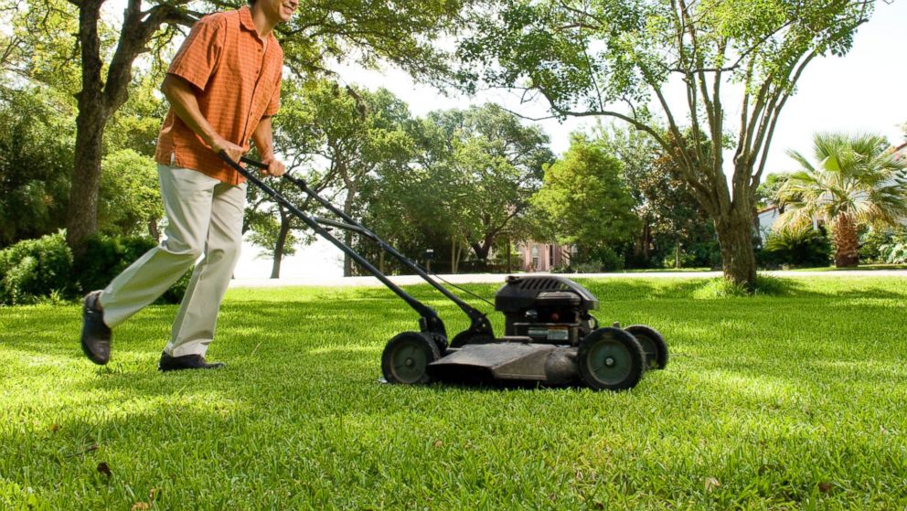 In this stock image, a man is pictured mowing a lawn. 