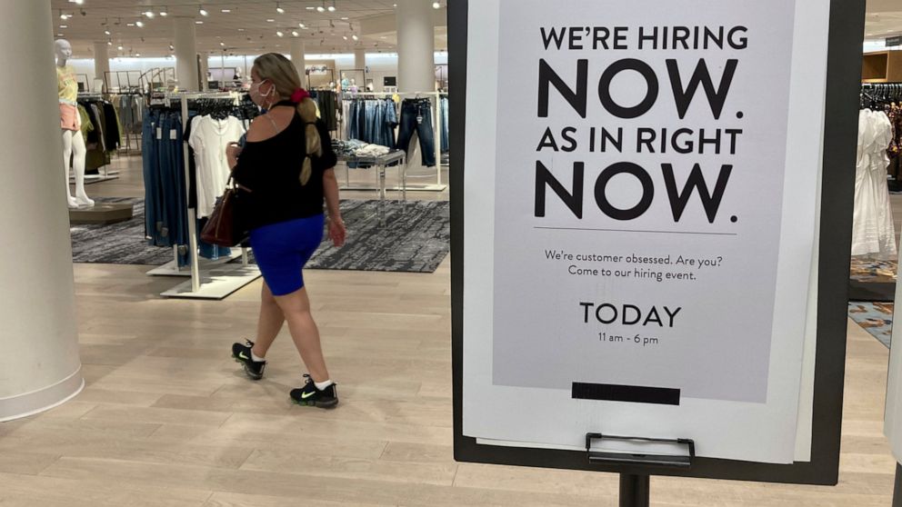 A customer walks behind a sign at a Nordstrom store seeking employees, Friday, May 21, 2021, in Coral Gables, Fla. The number of Americans seeking unemployment benefits dropped last week to 406,000, a new pandemic low and more evidence that the job m