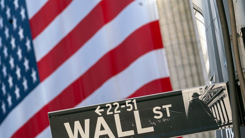 FILE - In this Monday, Sept. 21, 2020, file photo, a Wall Street street sign is framed by a giant American flag hanging on the New York Stock Exchange in New York. Stocks are falling in early trading on Wall Street Monday, Oct. 26, 2020, and deepenin