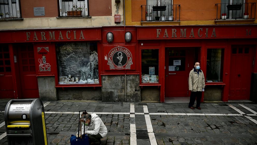 A man stands outside of a pharmacy wearing face protection during confinement to prevent the spread of coronavirus COVID-19, in Pamplona, northern Spain, Wednesday, April 8, 2020. COVID-19 causes mild or moderate symptoms for most people, but for som