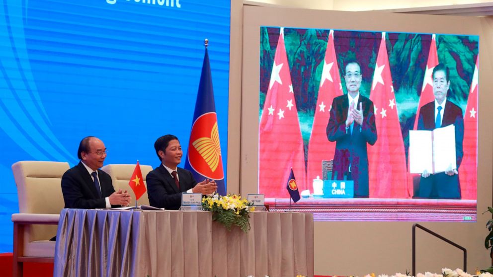 FILE - Vietnamese Prime Minister Nguyen Xuan Phuc, left, and Minister of Trade Tran Tuan Anh, right, applaud next to a screen showing Chinese Premier Li Keqiang and Minister of Commerce Zhong Shan holding up signed RCEP agreement, in Hanoi, Vietnam o
