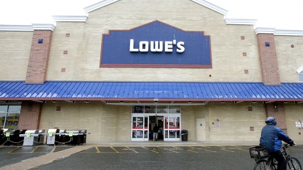 FILE- In this Feb. 23, 2018, file photo a cyclist rides near an entrance to a Lowe's retail home improvement and appliance store in Framingham, Mass. Lowe's Cos. is laying off thousands of employees at its U.S. stores as it outsources some of their d