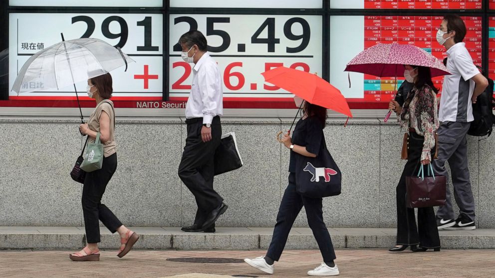 People wearing protective masks walk in the rain past an electronic stock board showing Japan's Nikkei 225 index at a securities firm Wednesday, Aug. 17, 2022, in Tokyo. Asian shares were mostly higher Wednesday as regional markets looked to strong e