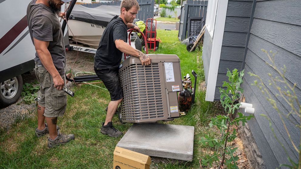 Carl Rocha, left, and Patrick Plummer, with Bills Heating & A/C Install air conditioning and a new furnace at a home on East Wabash Street, Wednesday, June 23, 2021, in Spokane, Wash. With temperatures forecast to hit over 100 degrees by Sunday, a ru