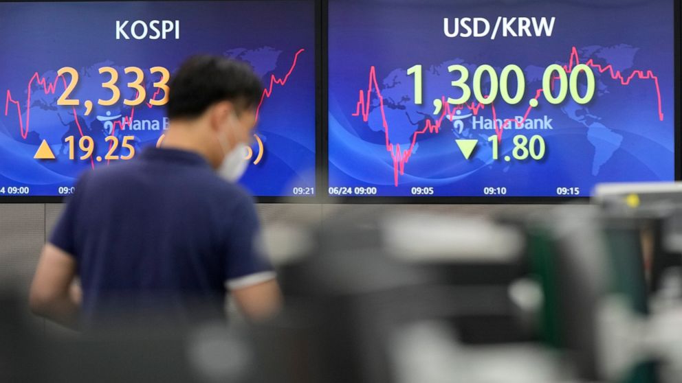 A currency trader walks by the screens showing the Korea Composite Stock Price Index (KOSPI), left, and the foreign exchange rate between U.S. dollar and South Korean won at a foreign exchange dealing room in Seoul, South Korea, Friday, June 24, 2022