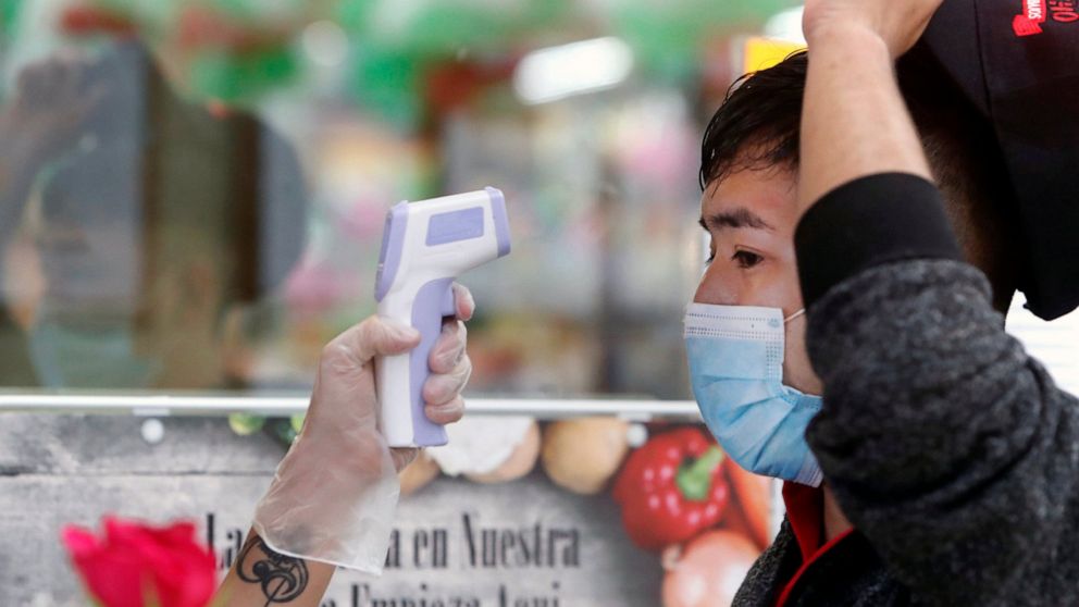FILE - In this May 12, 2020 file photo, amid concerns of the spread of COVID-19, Ronaldo Santos has his temperature checked before starting his work shift in the meat department of a grocery store in Dallas. With more businesses across the country ea