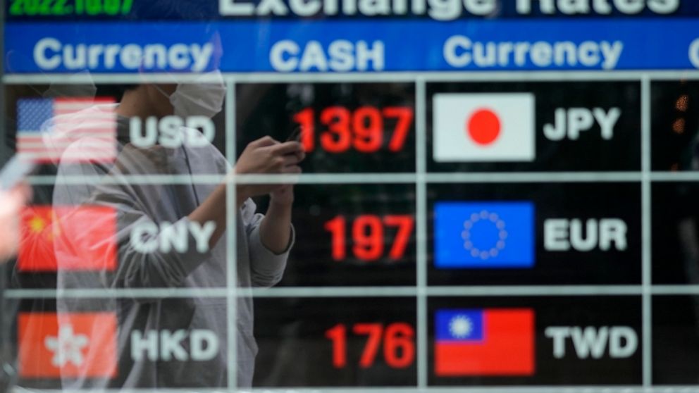 A man wearing a face mask is reflected on an electronic foreign currency exchange rates in downtown Seoul, South Korea, Friday, Oct. 7, 2022. Asian shares followed Wall Street lower Friday ahead of U.S. jobs data investors hope will persuade the Fede