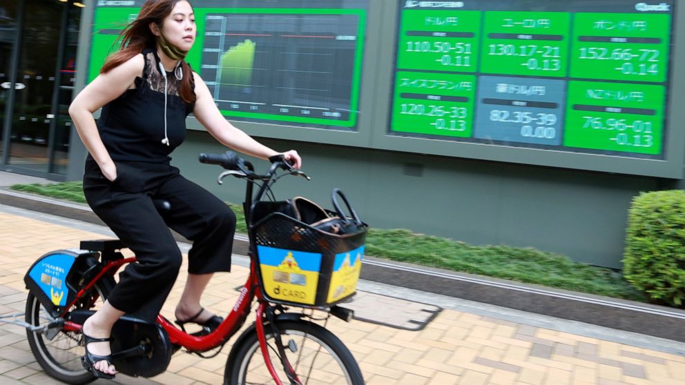 A woman cycles past an electronic stock board of a securities firm in Tokyo, Wednesday, July 14, 2021. Asian shares were mostly lower on Wednesday, tracking a decline on Wall Street as investors weighed the latest quarterly earnings reports from big 
