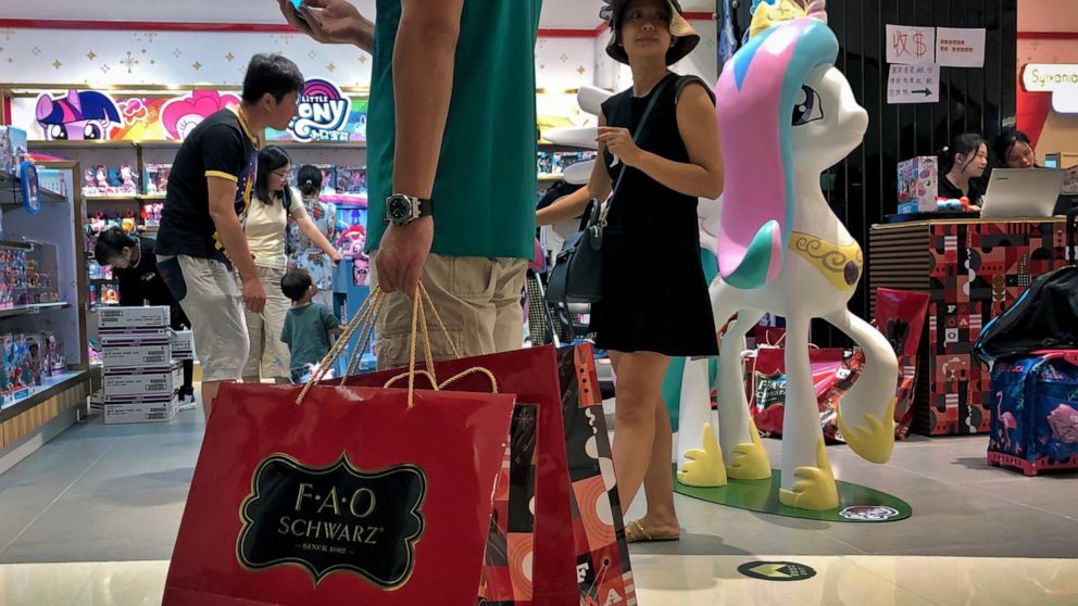 FILE - In this June 1, 2019, photo, file a man carries a paper bags containing toys purchased from the FAO Schwarz as people shop at the newly open FAO Schwarz toy store at the capital city's popular shopping mall in Beijing. Caught in the crossfire 