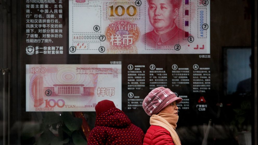 FILE - In a Monday, Feb. 18, 2019 file photo, women walk by a bank window panel displaying the security markers on the latest 100 Yuan notes in Beijing. The Trump administration has again decided not to label China or any other country as a currency 