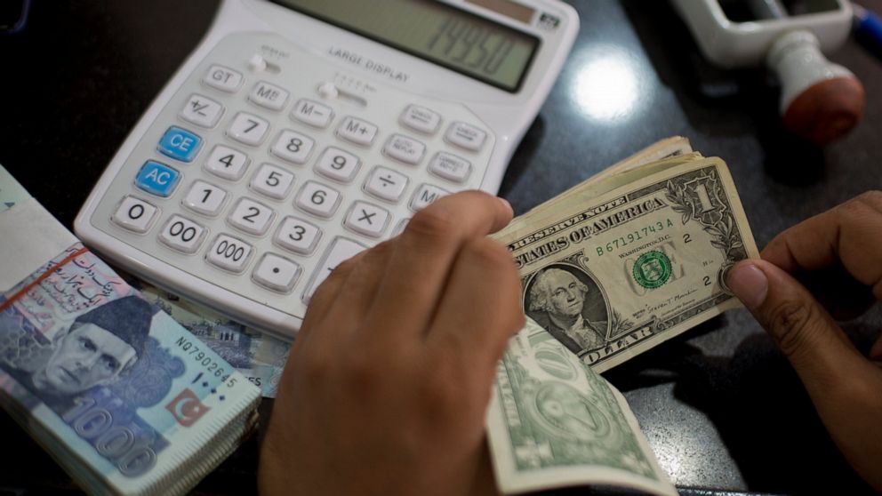 FILE - In this May 17, 2019, file photo US dollars are counted at a currency exchange in Islamabad, Pakistan. The global economy is slowing, largely because of the U.S. trade war with China, according to the 189-member International Monetary Fund. (A