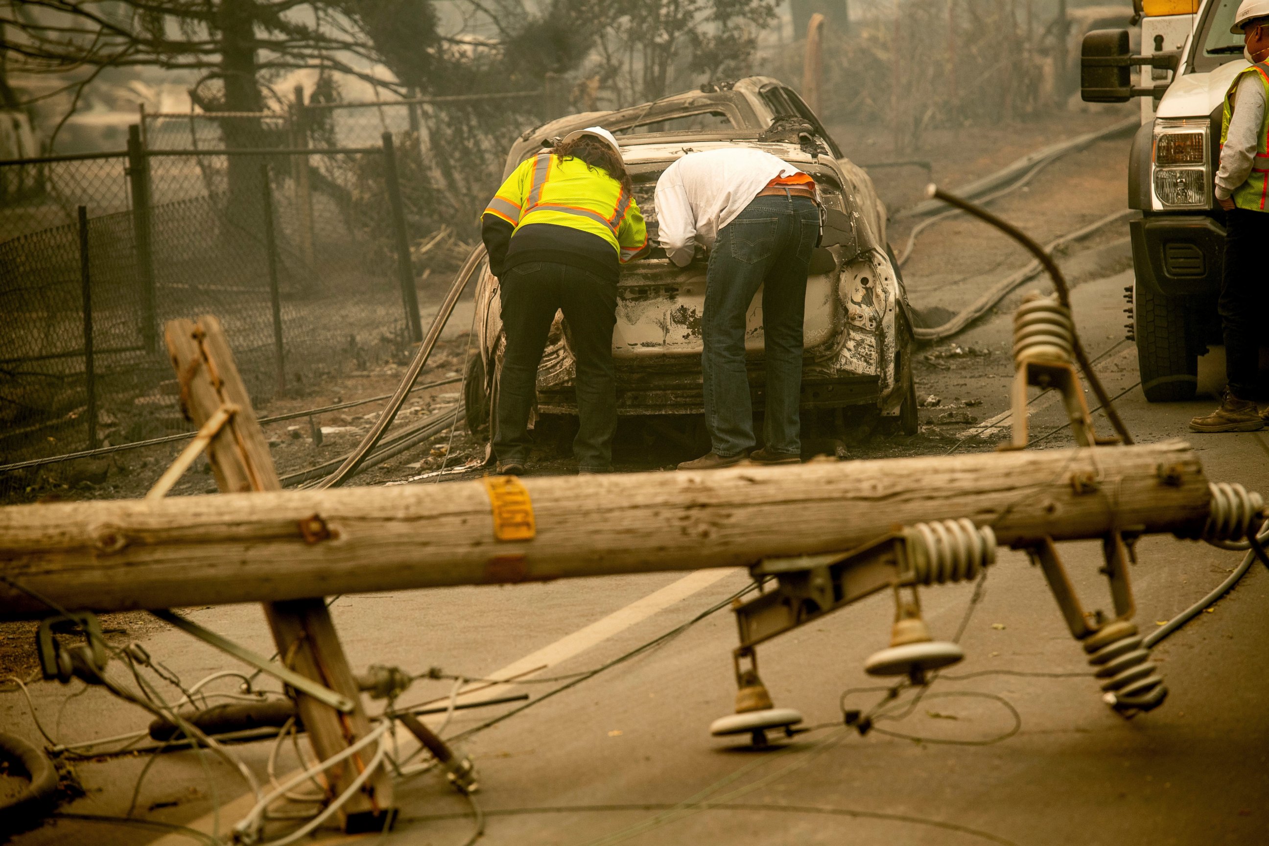 FILE - In this Nov. 10, 2018 file photo, with a downed power utility pole in the foreground, Eric England, right, searches through a friend's vehicle after the wildfire burned through Paradise, Calif. California’s largest utility company is getting b