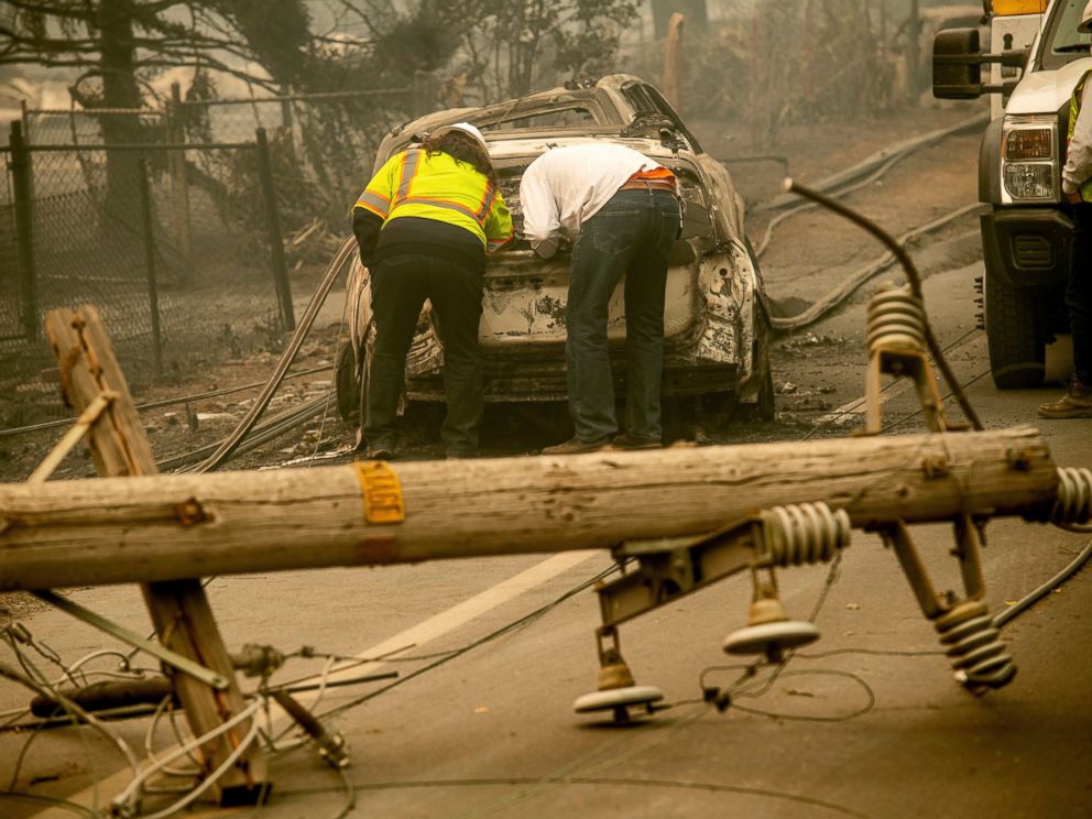 FILE - In this Nov. 10, 2018 file photo, with a downed power utility pole in the foreground, Eric England, right, searches through a friends vehicle after the wildfire burned through Paradise, Calif. California’s largest utility company is getting b