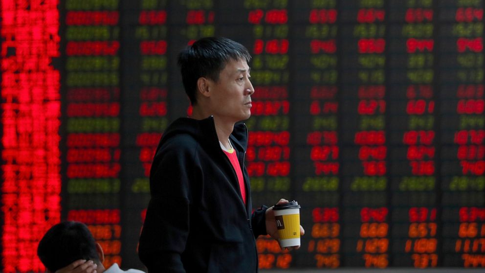 In this Thursday, Sept. 19, 2019, photo, a man holding a cup of coffee monitors the stock prices at a brokerage house in Beijing. Asian shares were mostly higher on Friday, Sept. 20, 2019 after a lackluster session on Wall Street, as investors shifte