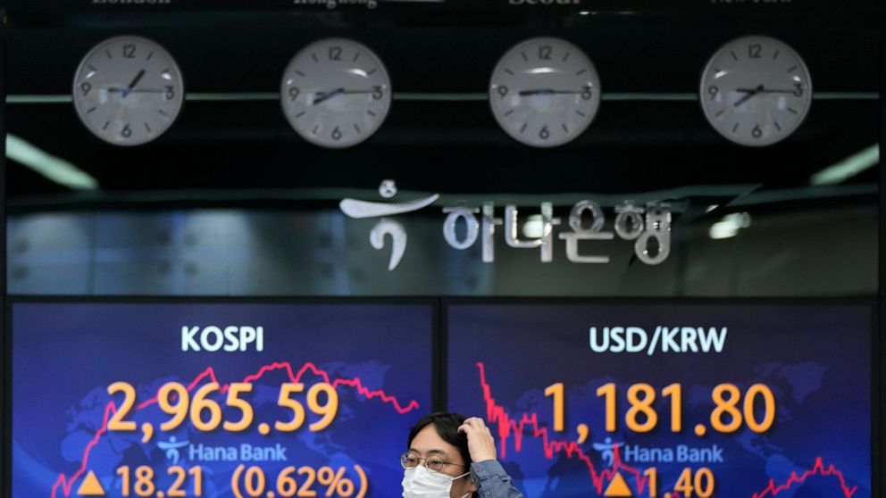 A currency trader passes by screens showing the Korea Composite Stock Price Index (KOSPI) and the foreign exchange rate between U.S. dollar and South Korean won, right, at the foreign exchange dealing room of the KEB Hana Bank headquarters in Seoul, 