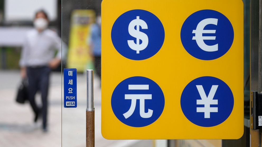 People wearing face masks walk by signs of foreign currency outside a money exchange office at a shopping district in Seoul, South Korea, Thursday, Aug. 12, 2021. Asian shares were mixed Thursday as caution set in among investors following another wo