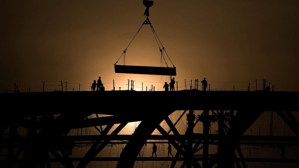 FILE - Workers are silhouetted against a sunset as they handle a steel frame on the roof of the Workers' Stadium under construction in Beijing, China, Monday, Feb. 28, 2022. China, the world’s top emitter of carbon dioxide and other greenhouse gases 