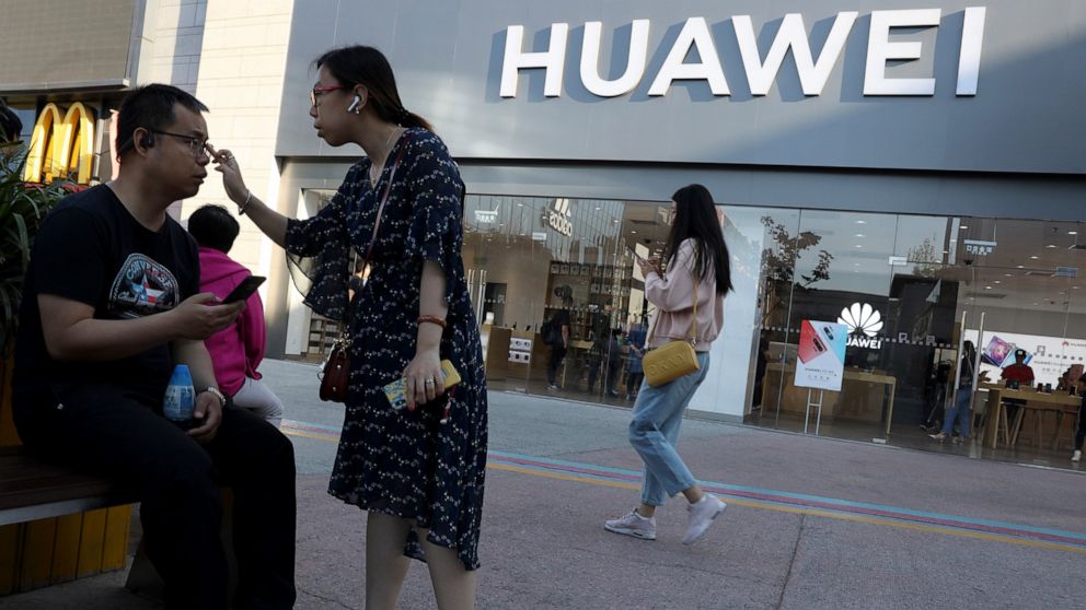 In this May 20, 2019, photo, a woman adjusts the glasses of a man outside a Huawei store in Beijing. The world's largest association of technology professionals has reversed a decision that would have excluded employees of Chinese tech giant Huawei a