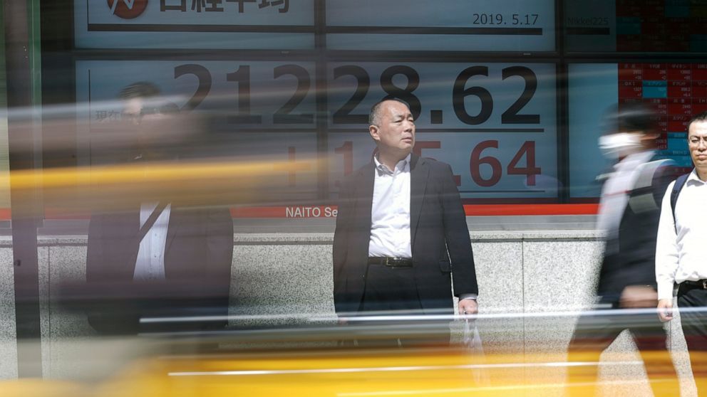 People walk past an electronic stock board showing Japan's Nikkei 225 index at a securities firm in Tokyo Friday, May 17, 2019. Asian stocks were mixed on Friday amid worries that U.S. economic sanctions on Huawei would put a drag on trade negotiatio