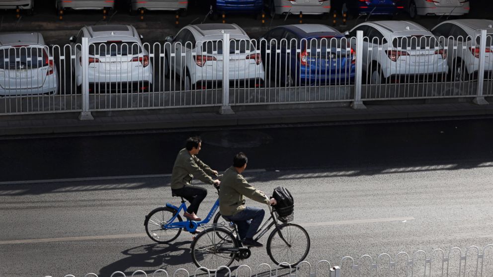 People ride bicycles past new Honda cars stored underneath an overpass in Beijing, Thursday, March 14, 2019. The downturn in China's auto market worsened in January and February as an economic slowdown and a tariff fight with Washington chilled deman