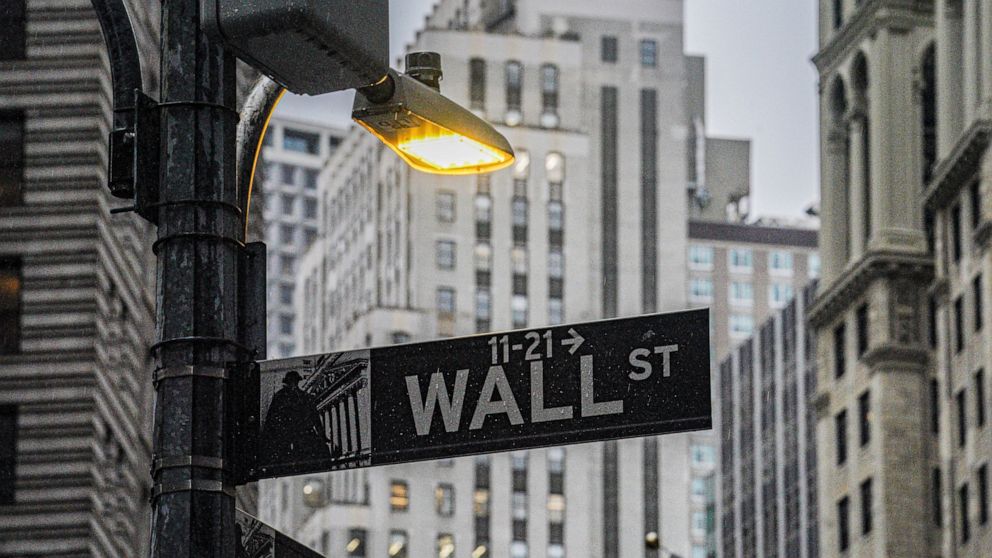 FILE - A street light brightens a Wall Street sign outside the New York Stock Exchange, Oct. 3, 2022, in New York. Stocks wavered between gains and losses in early trading on Wall Street, leaving indexes mixed as another batch of companies reported t