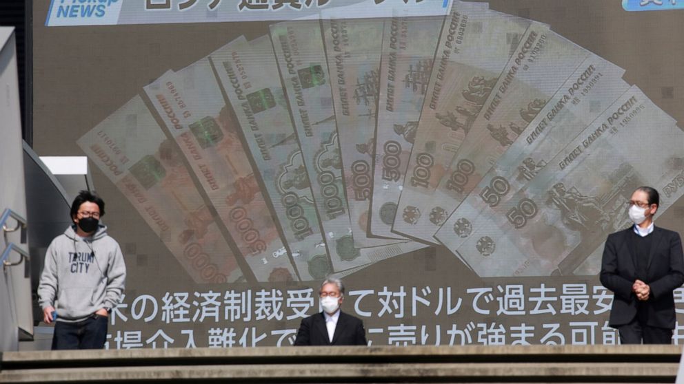 FILE - People walk in front of a huge TV screen showing banknotes of Russian ruble in Tokyo, Tuesday, March 1, 2022. Russia said Wednesday, April 6, that it made a debt payment in rubles this week, a move that may not be accepted by Russia’s foreign 