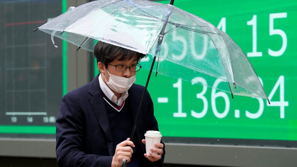 A man wearing a protective mask walks in front of an electronic stock board showing Japan's Nikkei 225 index at a securities firm Tuesday, Dec. 14, 2021, in Tokyo. Stocks were mostly lower in Asia on Tuesday after Wall Street retreated from recent re
