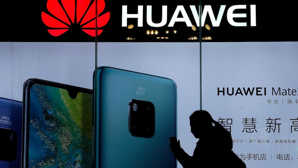 FILE - In this Dec. 11, 2018, file photo, a woman browses her smartphone as she walks by a Huawei store at a shopping mall in Beijing. China’s government has accused Washington of trying to block its industrial development after Vice President Mike P
