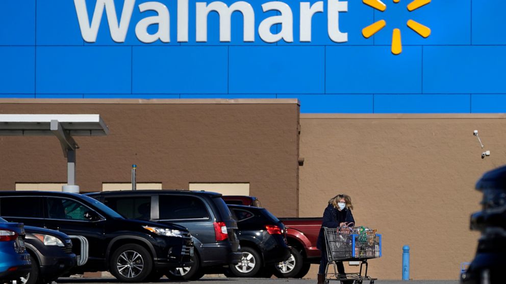 FILE - A woman wheels a cart with her purchases out of a Walmart, on Nov. 18, 2020, in Derry, N.H. On Monday, July 25, 2022, Walmart Inc., lowered its profit outlook for the second quarter and the full year, citing surging inflation on basics like fo