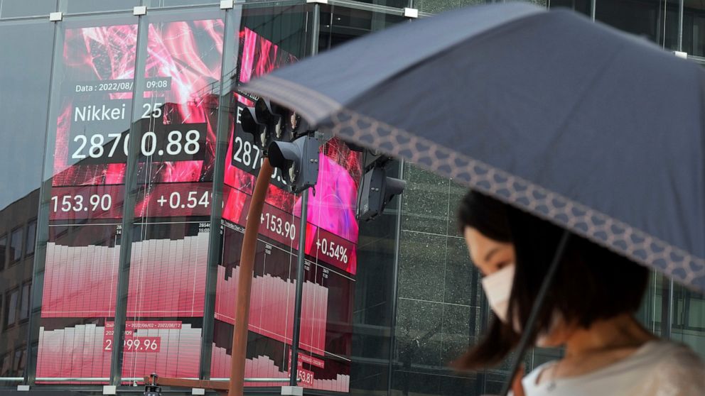 A person wearing a protective mask walks past an electronic stock board showing Japan's Nikkei 225 index at a securities firm Monday, Aug. 15, 2022, in Tokyo. Shares were mixed in Asia on Monday after China's central bank cut a key interest rate and 