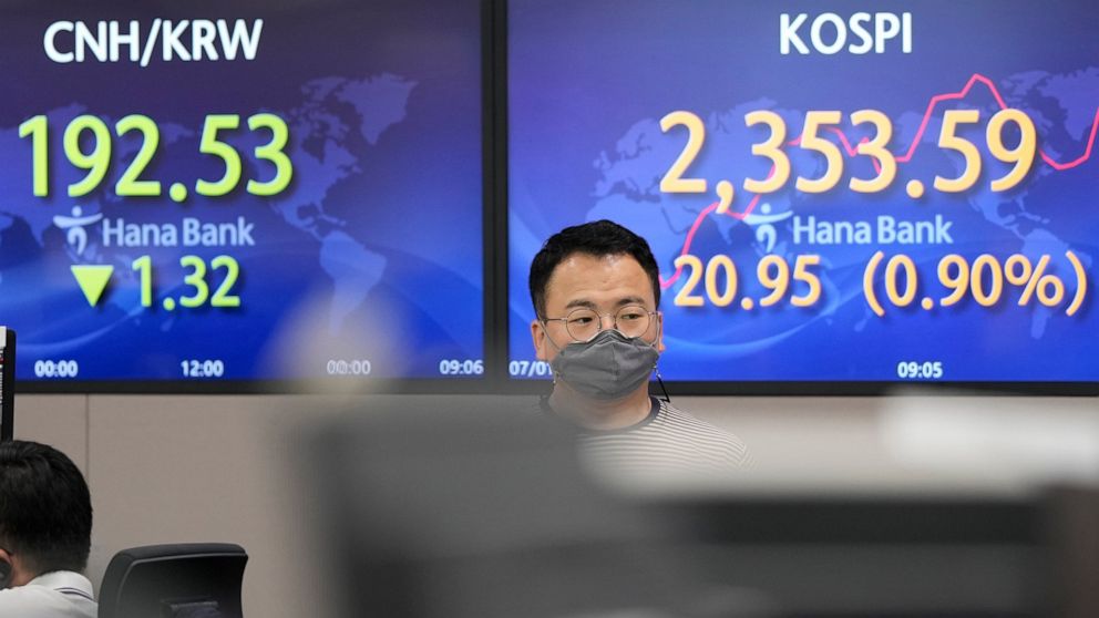 A currency trader walks by the screens showing the Korea Composite Stock Price Index (KOSPI), right, and the foreign exchange rate at a foreign exchange dealing room in Seoul, South Korea, Friday, July 1, 2022. Asian benchmarks were mostly lower on F