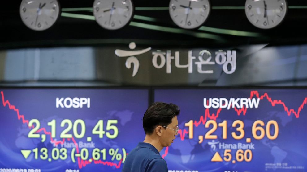 A currency trader walks by the screens showing the Korea Composite Stock Price Index (KOSPI), left, and the foreign exchange rate between U.S. dollar and South Korean won at the foreign exchange dealing room in Seoul, South Korea, Friday, June 19, 20