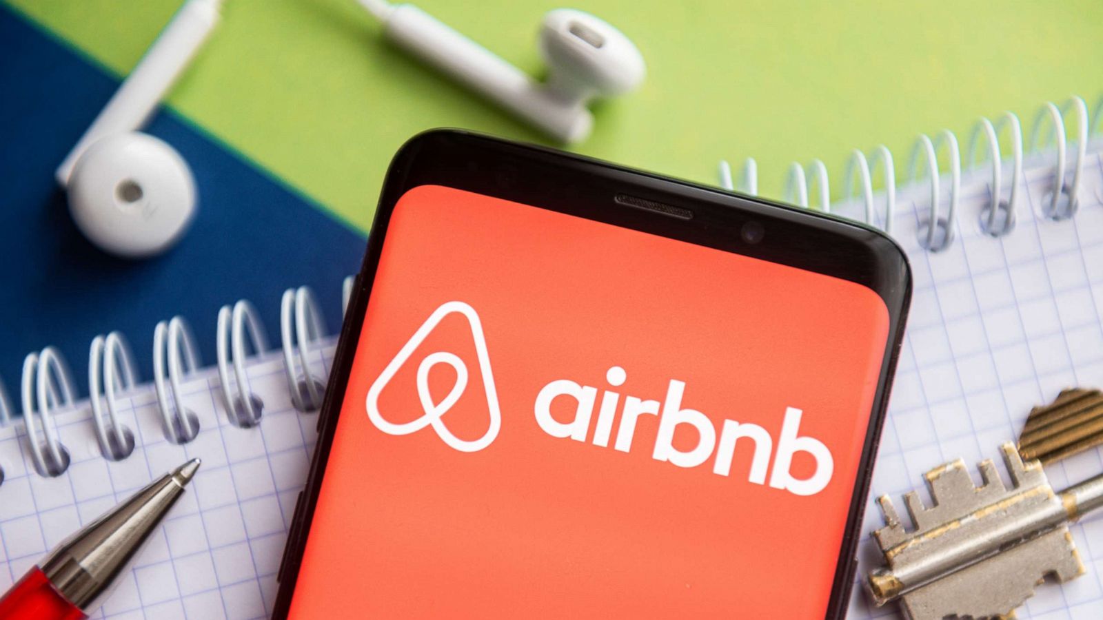 PHOTO: An Airbnb logo is seen displayed on a smartphone with a pen, key, book and headsets in the background in this undated stock photo.