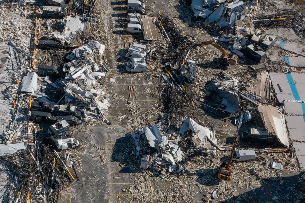 PHOTO: Debris is gathered and moved in to piles by excavators around damaged delivery vehicles where crews are performing search and recovery operations at an Amazon distribution center in Edwardsville, Ill., Dec. 12, 2021.