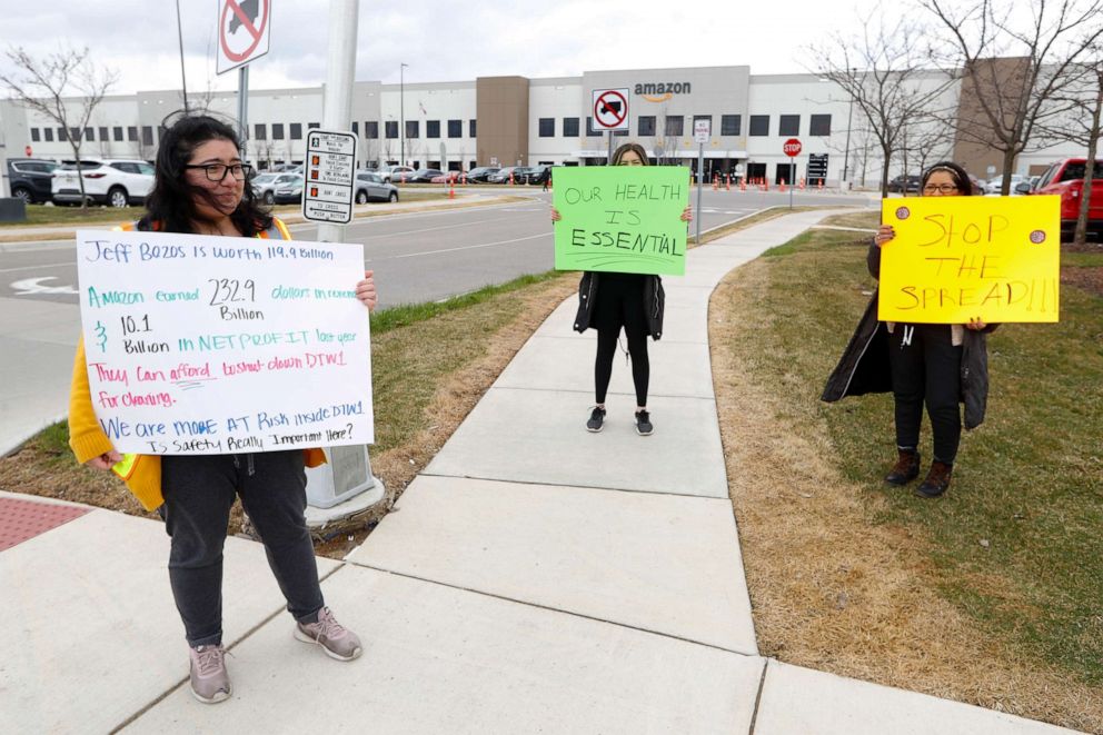 PHOTO: Breana Avelar, left, a processing assistant and family members, hold signs outside the Amazon DTW1 fulfillment center in Romulus, Mich., April 1, 2020.