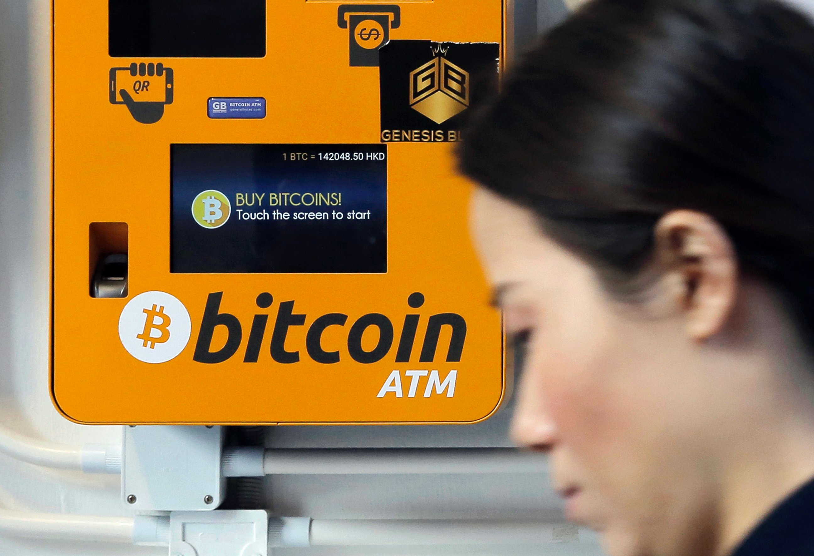 FILE - In this Dec. 21, 2017 file photo, a woman walks past the Bitcoin ATM in Hong Kong.