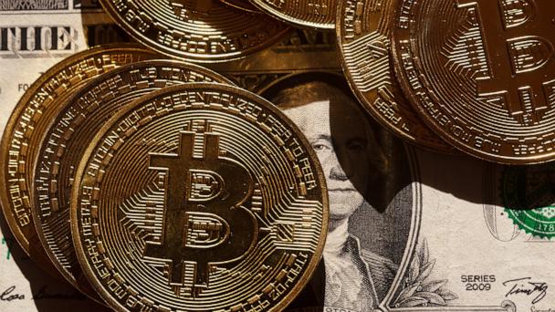 Golden Bitcoin coins lie on a US dollar banknote.