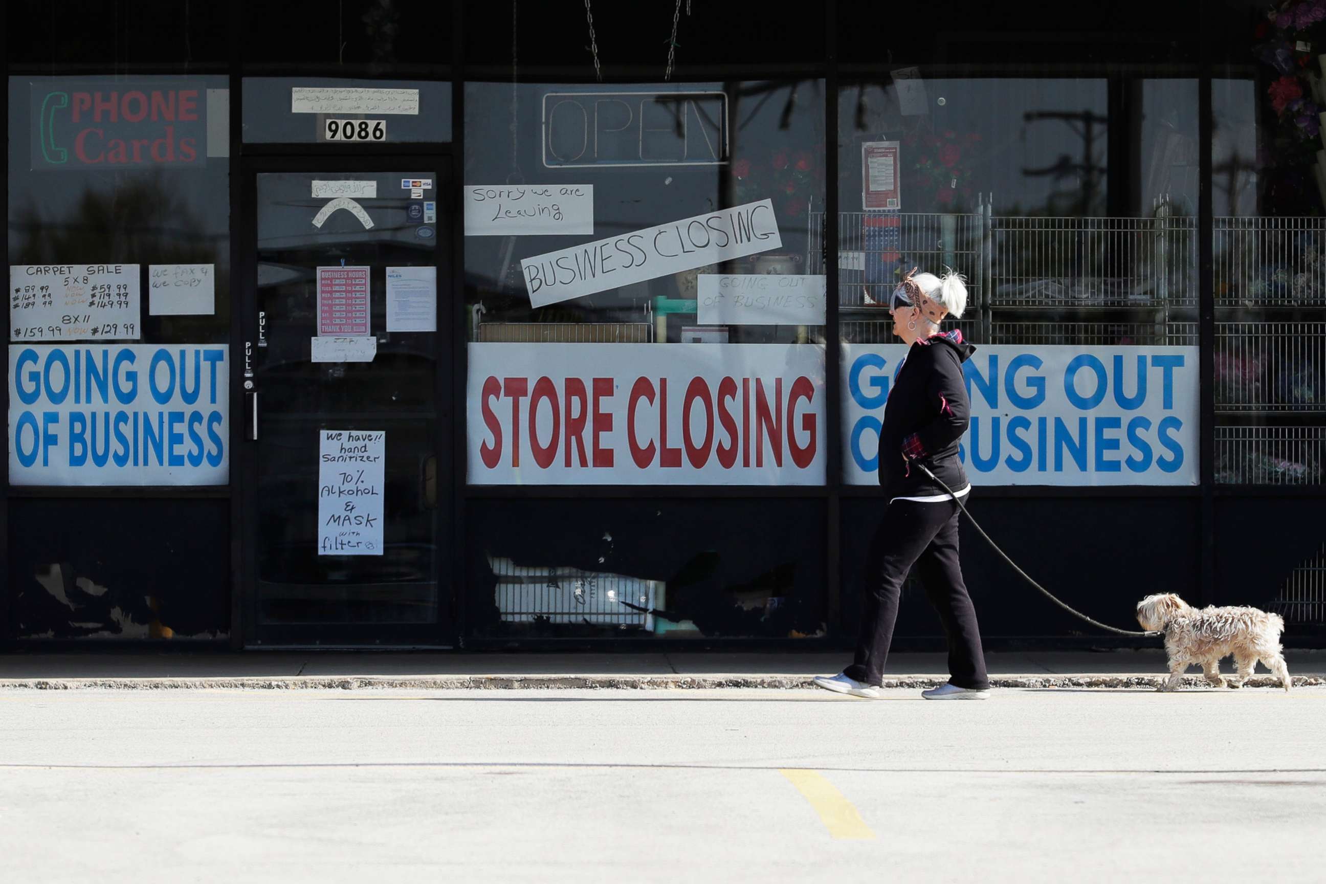 PHOTO: A woman takes walk with a dog in front of the closing signs displayed in a store's window front in Niles, Ill., May 13, 2020.