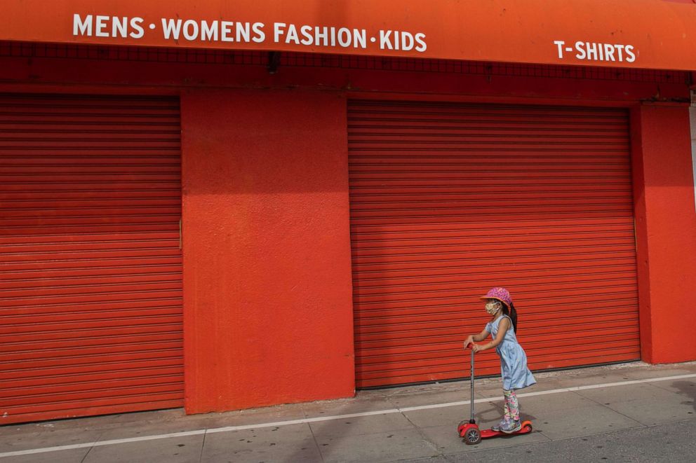 PHOTO: A girl rides a scooter passed the closed stores on the boardwalk in Venice, Calif., April 26, 2020. 