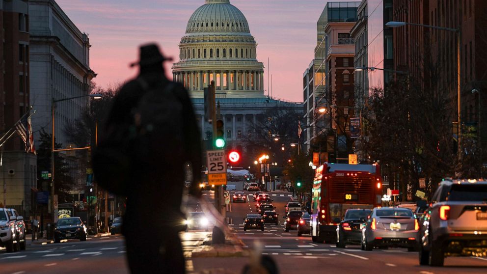 PHOTO: A man walks his dog as the sun rises over the U.S. Capitol, Dec. 28, 2020 in Washington, D.C.