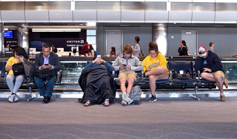 PHOTO: In this June 12, 2019, file photo, passengers waiting for their flight to board sit in the terminal and use their smartphones at Denver International Airport in Denver.
