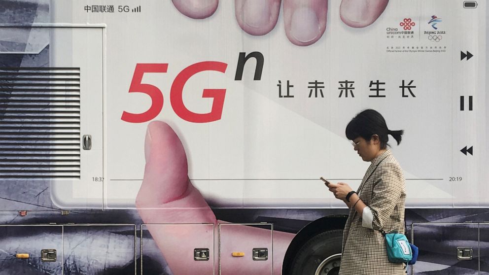 PHOTO: A woman using her mobile phone walks past a vehicle covered in a China Unicom 5G advertisement in Beijing, China, Sept. 17, 2019.