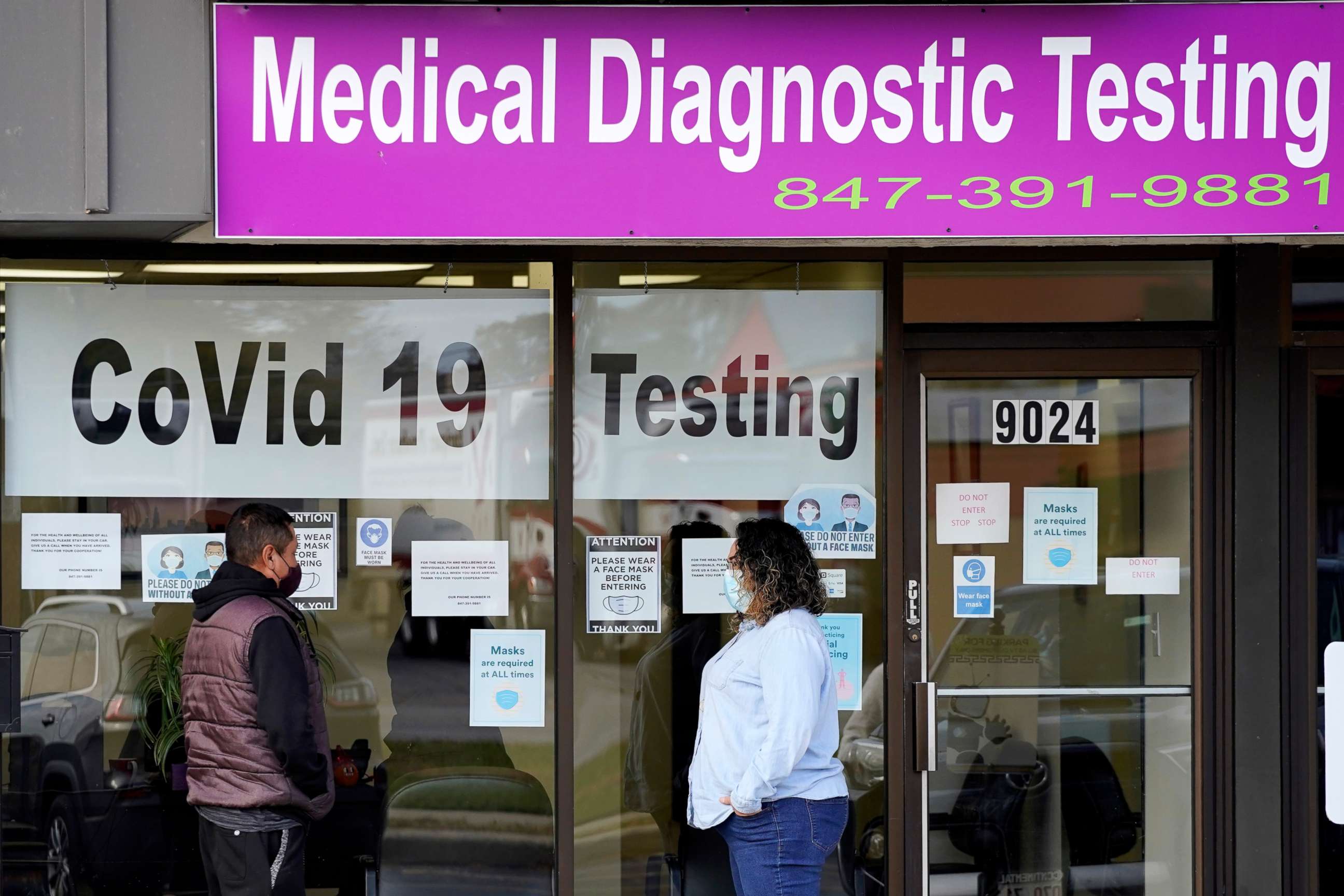 PHOTO: An Exam Corp Lab employee, right, wears a mask as she talks with a patient lined up for COVID-19 testing in Niles, Ill., Oct. 21, 2020.