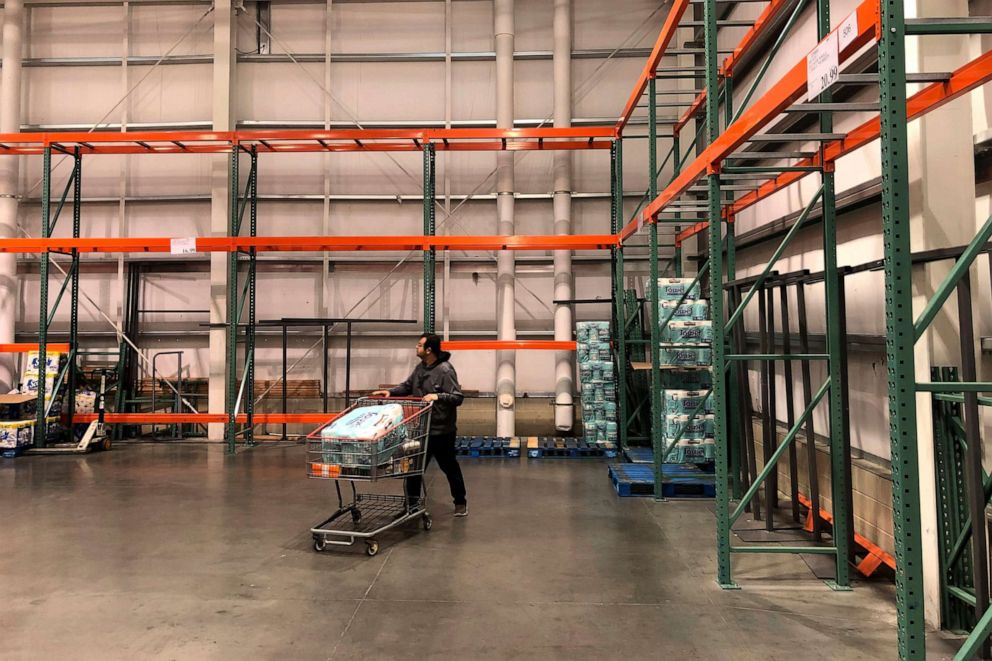 PHOTO: In this March 2, 2020, file photo, a customer walks past mostly empty shelves that normally hold toilet paper and paper towels at a Costco store in Teterboro, N.J.