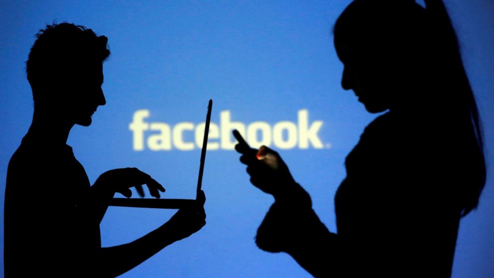 PHOTO: People are silhouetted as they pose with laptops in front of a screen projected with a Facebook logo, in this picture illustration, Oct. 29, 2014. 