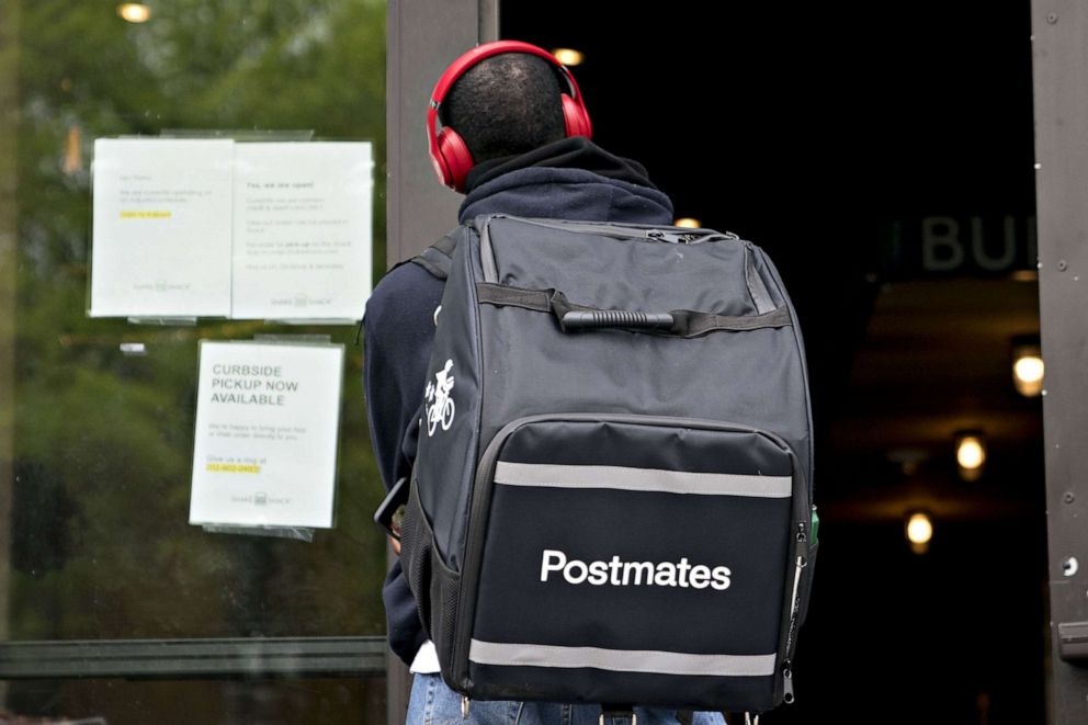 PHOTO: A Postmates Inc. delivery person stands outside a restaurant in Washington, D.C., on April 20, 2020.
