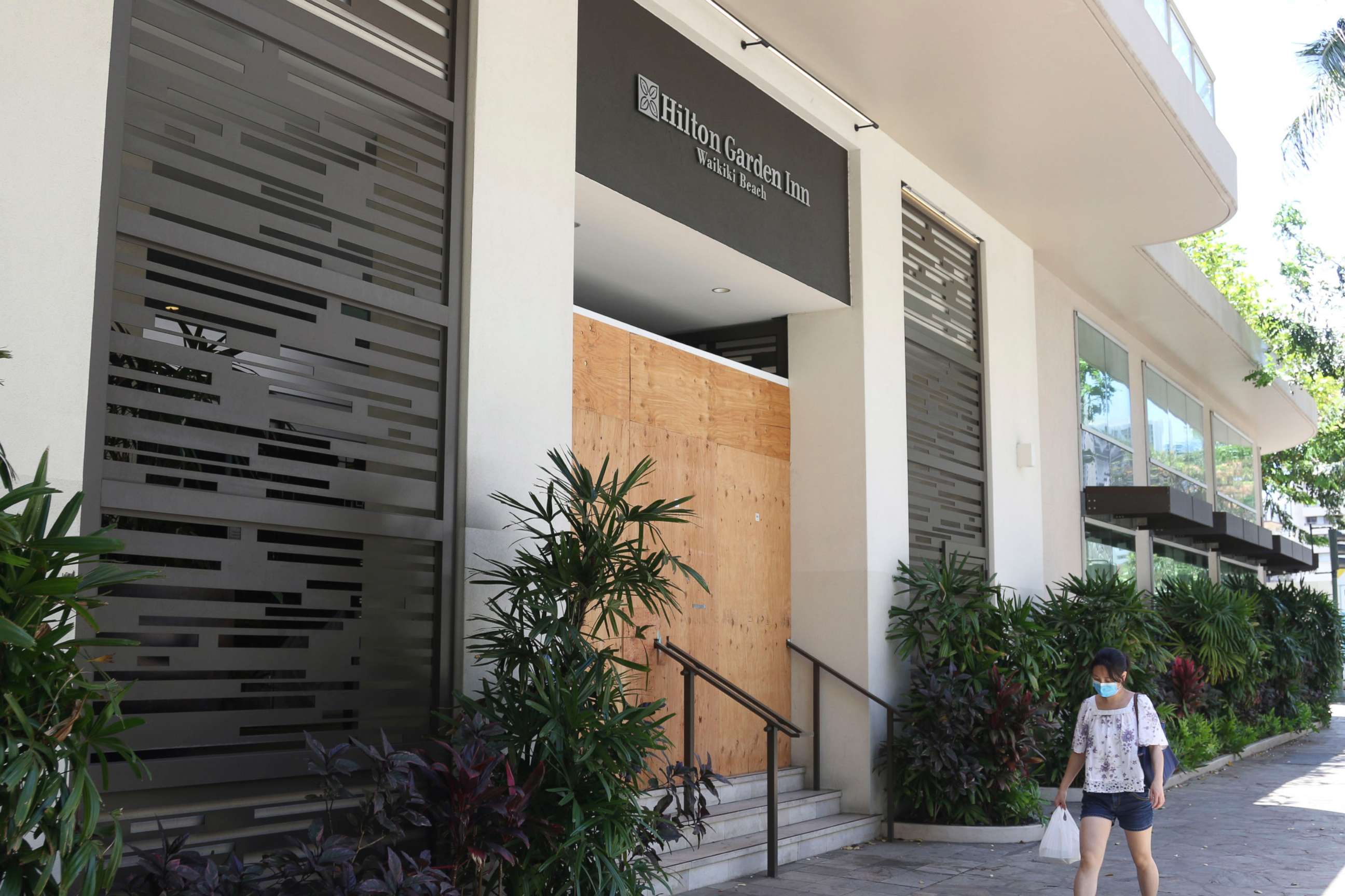 PHOTO: In this photo taken June 5, 2020, a woman walks past the closed doors of the Hilton Garden Inn hotel in Honolulu.